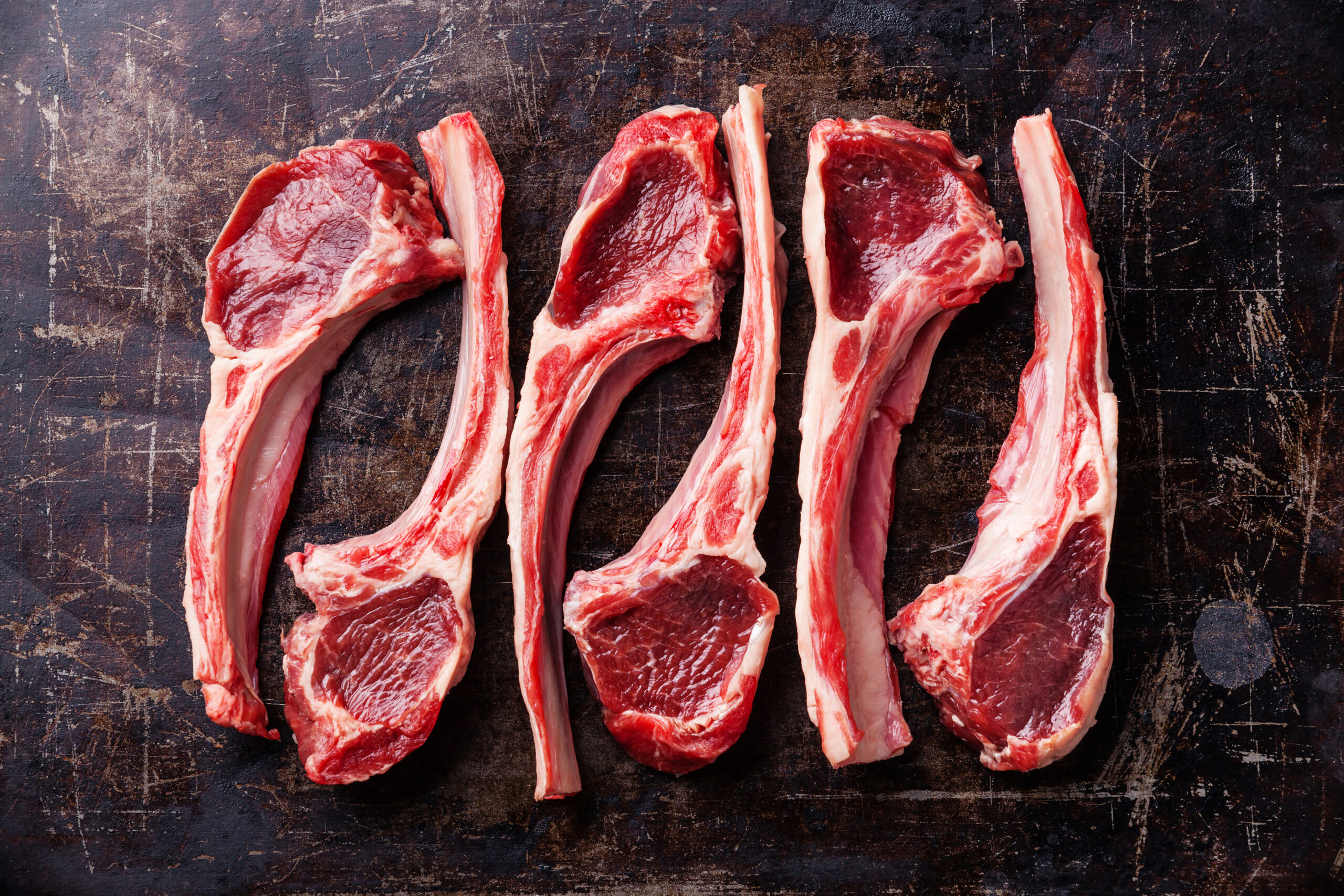 Raw fresh lamb ribs on dark background Fresh raw lamb chops arranged on a rustic wooden cutting board, showcasing rich red meat and marbled fat, ideal for grilling or roasting.